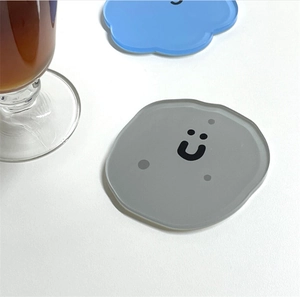 Nahaufnahme eines grauen Acryl-Untersetzers mit niedlichem Smiley auf weißem Tisch