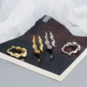 Detailed view of polished gold and silver irregular wavy hoop earrings on a textured surface