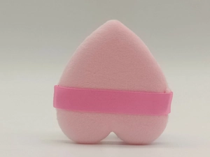Detail of pink heart-shaped powder puff with ribbon handle and plush texture