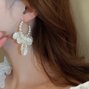 Detailed view of elegant pearl hoop earrings with white petals on model's ear