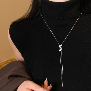 Dettaglio di collana lunga argentata con nappa e ciondolo a Z con zirconi su maglia nera