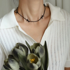 Close-up of black beaded necklace with bow detail worn by a model on white polo shirt