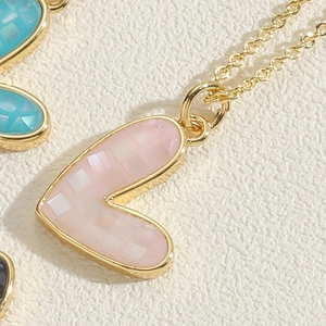 Macro detail of a heart pendant with pink shell inlay and golden grid texture finish