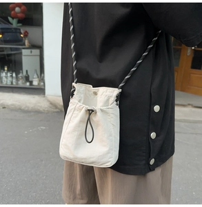 Detail of off-white drawstring crossbody phone bag with black and white woven strap