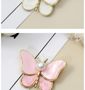 Close-up of golden butterfly brooches featuring pink and white inlay with faux pearls
