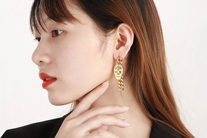 Macro detail of a gold skull charm and Cuban link chain drop earring on model