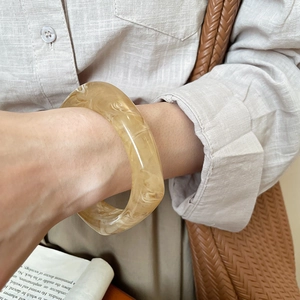 Detail of wide resin bangle with amber marble texture worn on model with linen shirt