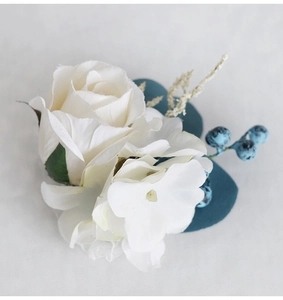 Detailed view of white silk rose boutonniere with blue berries and teal leaves