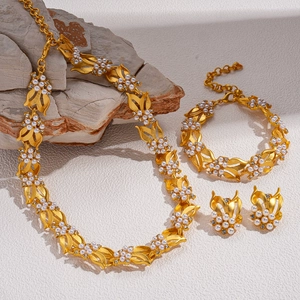 Set collana dorata con perle bianche e foglie su sfondo materico in pietra naturale
