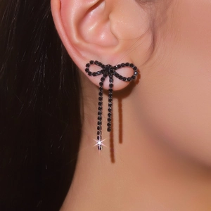 Close-up of elegant black bow earrings with long shimmering tassels on model