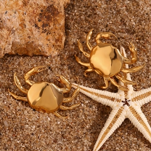 Detailed macro view of gold-plated crab studs on a natural beach with a white starfish