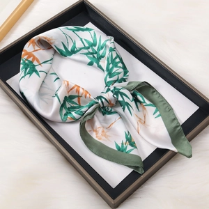 Detailed view of square silk scarf with bamboo leaf prints and green stitched edges