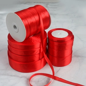 Detailed view of red satin ribbon rolls in three sizes on a grey marble background