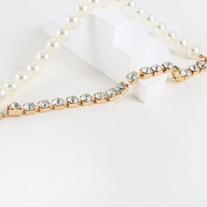 Detail of gold chain with rhinestones and white pearls with OT buckle closure