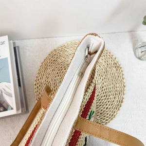 Large woven straw shoulder bag with red stripes and premium leather straps on a white desk