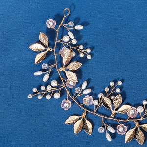 Gold bridal headband with metal leaves, pearls, and pink rhinestone flowers on blue surface
