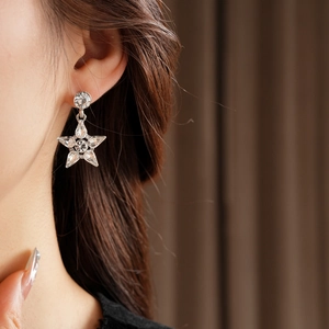 Close-up of star-shaped silver drop earrings with crystals worn by a model