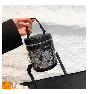 Detail of black cylindrical bucket bag featuring white embroidery and silver zipper closure
