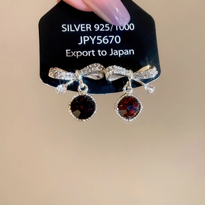 Detailed close-up of 925 silver bow earrings with crystals and a red round gemstone