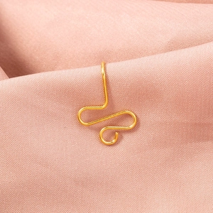 Close-up of golden butterfly-shaped stainless steel nose clip on pink fabric background