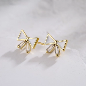 Golden bow earrings with white enamel and clear cubic zirconia on white marble base
