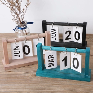 Three wooden flip perpetual calendars in wood, black, and peacock blue on a desk