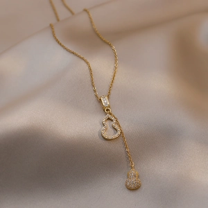 Collier en acier doré avec pendentifs double gourde et zircons sur fond de soie champagne