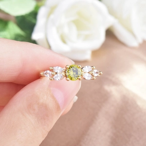 Olive green zircon ring with gold band held against a luxury floral background