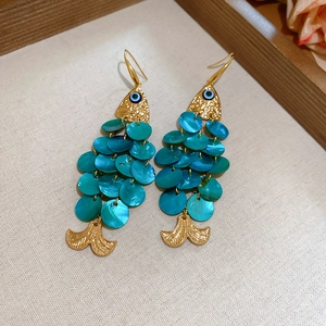 Macro detail of gold fish earrings with teal scales and protective evil eye charms