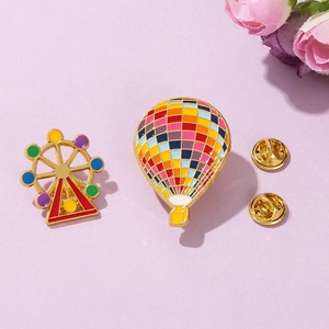 Detail of hot air balloon and Ferris wheel enamel pins with golden metal base