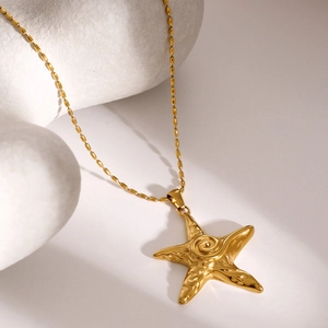 Macro view of golden bead chain necklace featuring a starfish pendant on stone