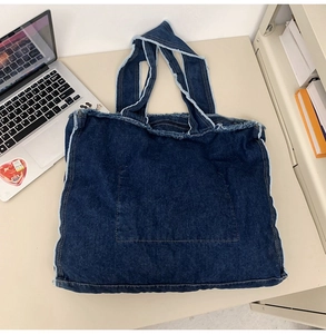 Detail of dark blue denim tote bag with vintage frayed edges and a front pocket