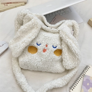 Dettaglio borsa a tracolla in peluche bianca con ricami e accessori per laptop