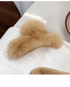 Close-up of soft camel rabbit fur claw clip on textured white fabric background