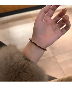 Dettaglio del bracciale in pelle intrecciata rossa con accenti dorati su manica morbida