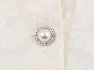 Détail d'un bouton perle rond avec bordure tressée argentée sur tissu en dentelle blanche