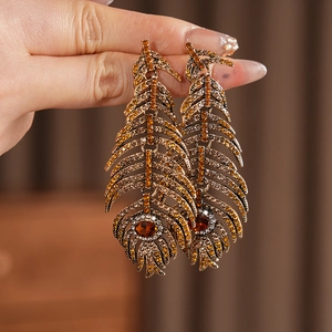 Detailed close-up of vintage bronze feather earrings with sparkling amber rhinestones