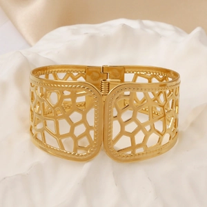 Detailed macro view of wide golden bangle with geometric hollow cutouts and spring hinge