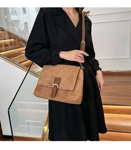 Detail of a brown suede crossbody bag with flap closure and adjustable leather strap