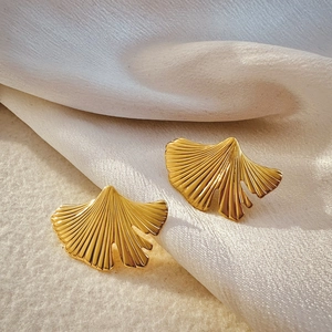 Macro detail of 18K gold ginkgo leaf earrings with brushed metal texture on silk