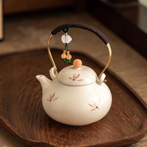 Beige ceramic teapot with orchid pattern and rope-wrapped handle on a wooden tray