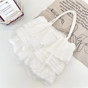 Dettaglio delle balze in pizzo e del ricamo floreale su una borsa tote in cotone bianco