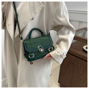 Detail of dark green crocodile texture bag with gold lock on a beige coat background