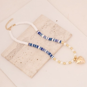 Detail of bohemian clay bead necklace with pearls and gold heart pendant on stone