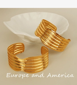 Detailed view of a wide gold wavy cuff bracelet layered with metallic fluid design