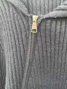 Detail of premium ribbed knit texture and a golden zipper pull on a black cardigan