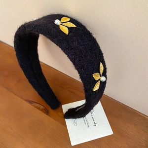 Detail of black velvet headband with gold metal leaves and white pearls on wooden surface