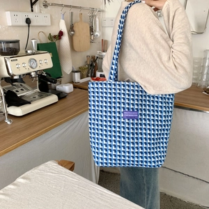 Detail of blue plaid canvas tote bag showing knit texture and purple logo label