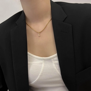 Gros plan du collier en acier titane doré avec un pendentif lettre L en cristaux