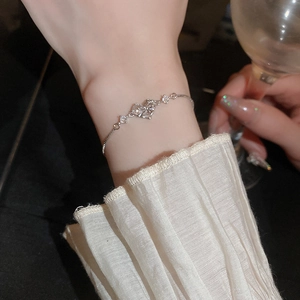 Silver metal heart bracelet with bow and zircons shown on wrist in elegant evening setting
